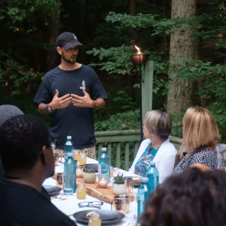 a man is standing at a table with people around him a man is standing at a table with people around him